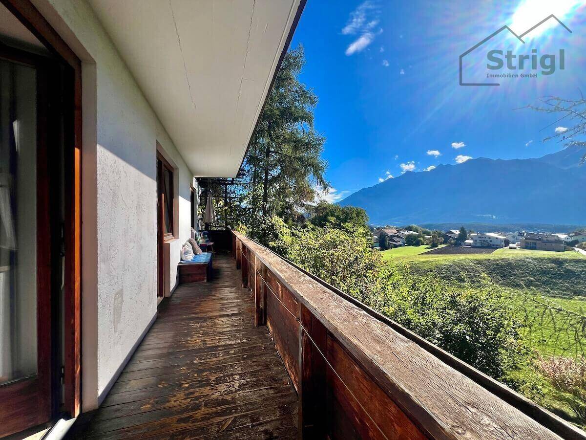 Langer Holzbalkon mit weitem Blick über die grüne Landschaft und die umliegenden Berge.