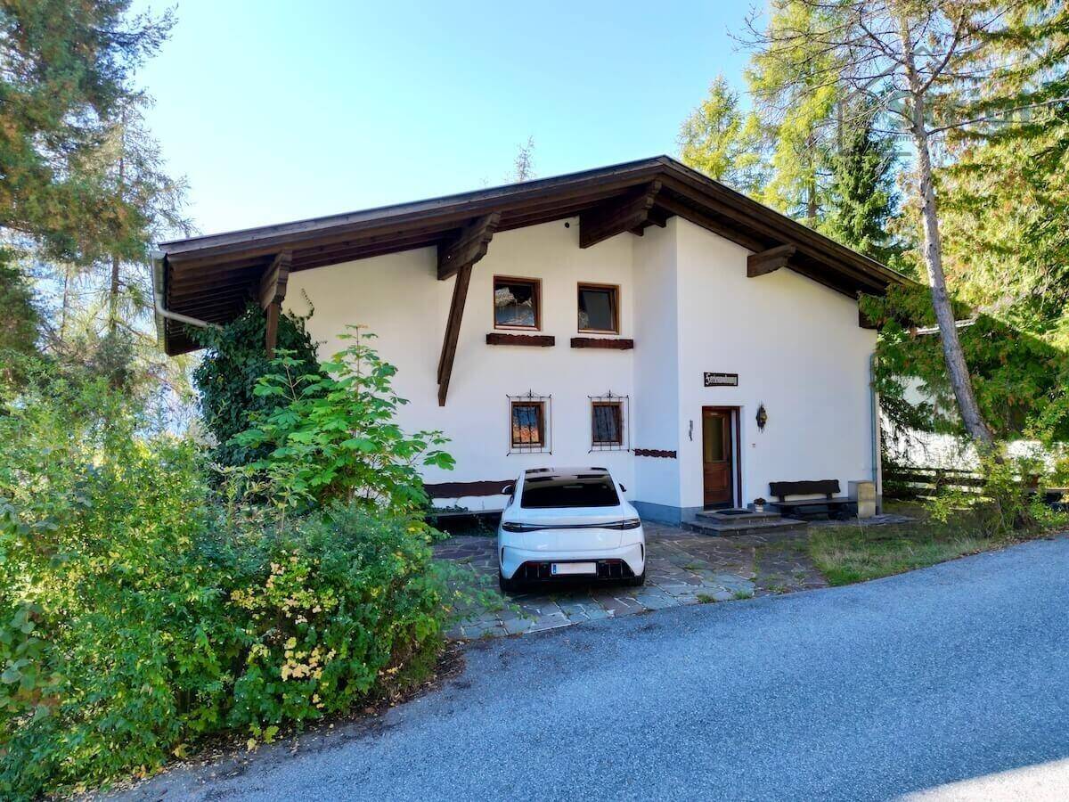 Vorderansicht eines charmanten Hauses mit weißer Fassade, Holzelementen und einem gepflasterten Vorplatz.
