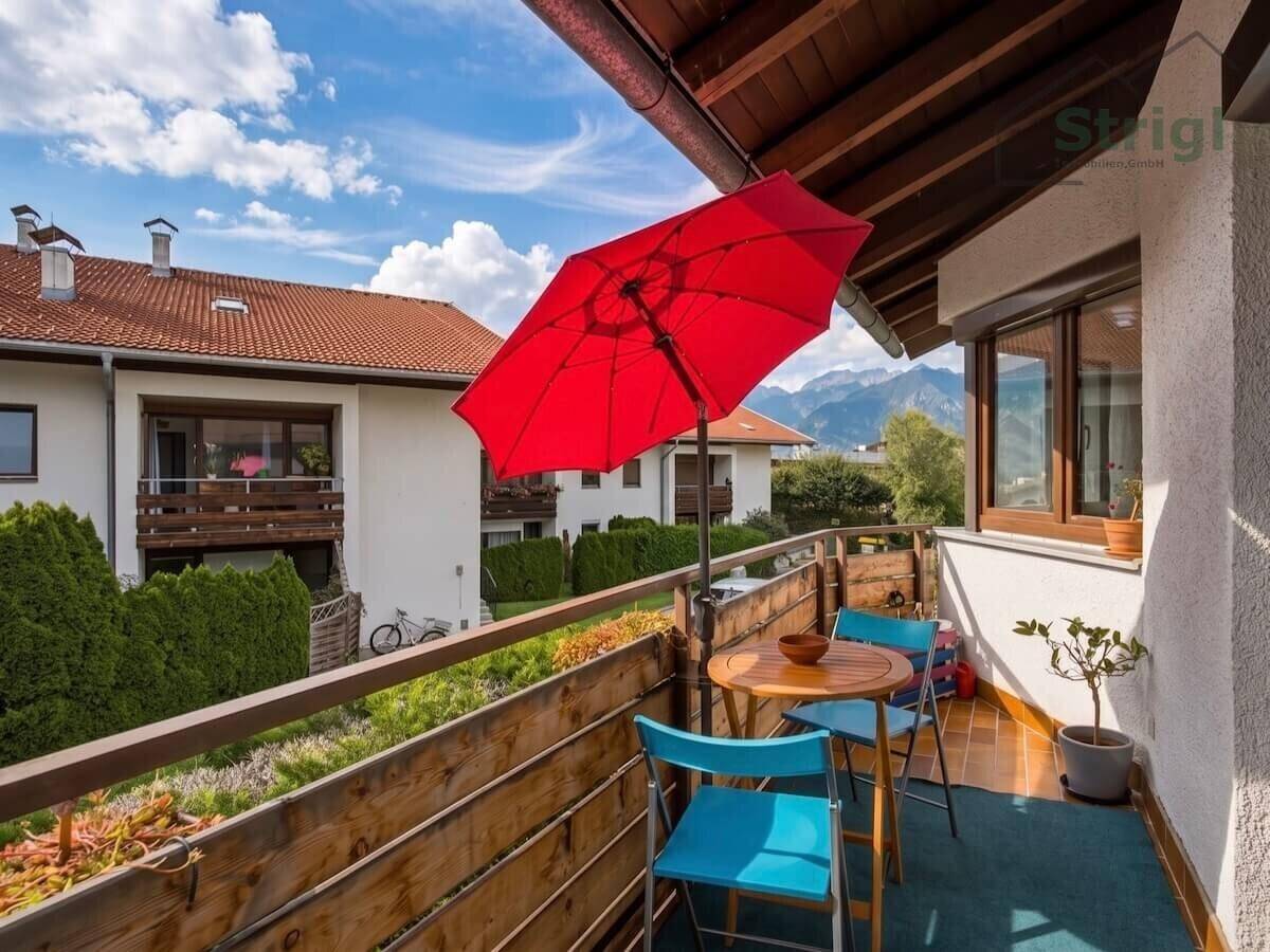 Sonniger Balkon mit Sitzgelegenheiten, rotem Sonnenschirm und Bergblick.