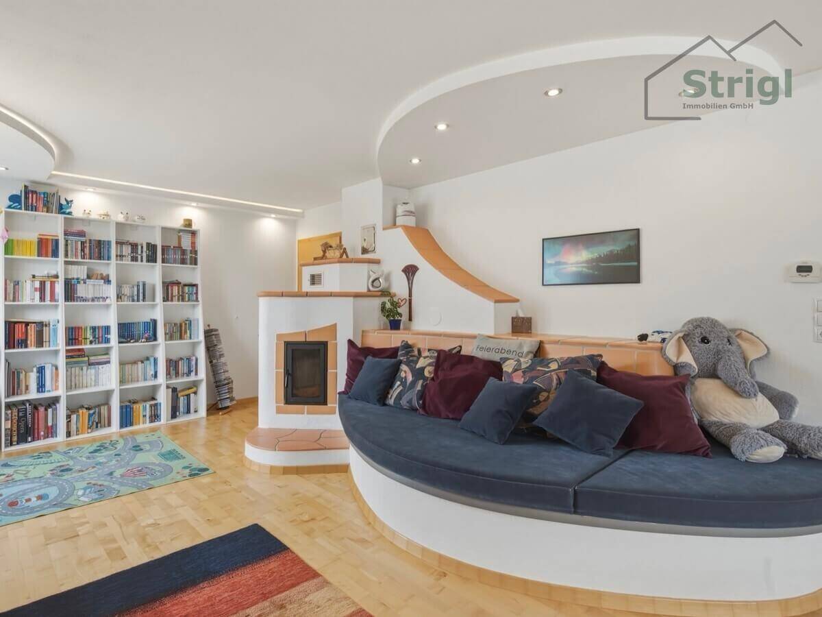 Heller Wohnbereich mit großem Bücherregal, integriertem Sofa und Kachelofen.
