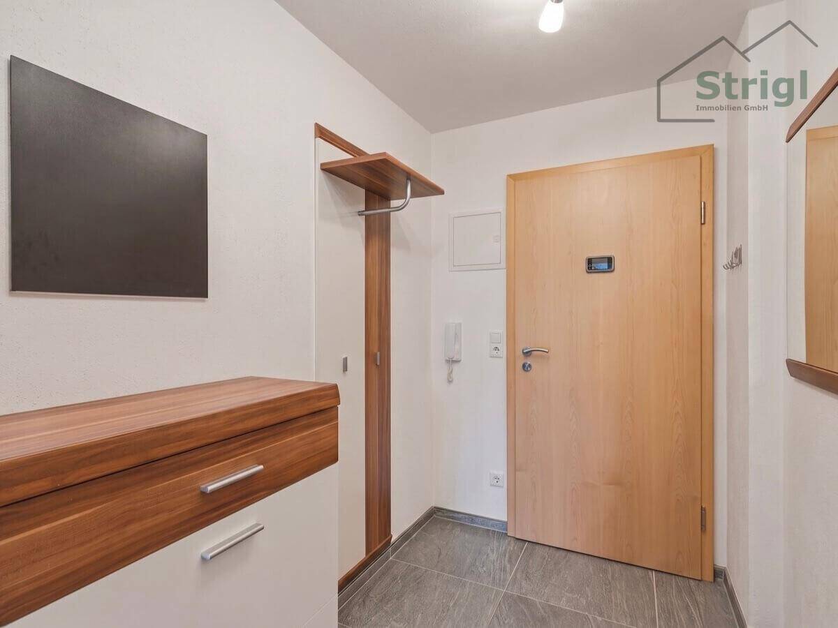 Heller Eingangsbereich mit Holzmöbeln, Garderobe und Fliesenboden.