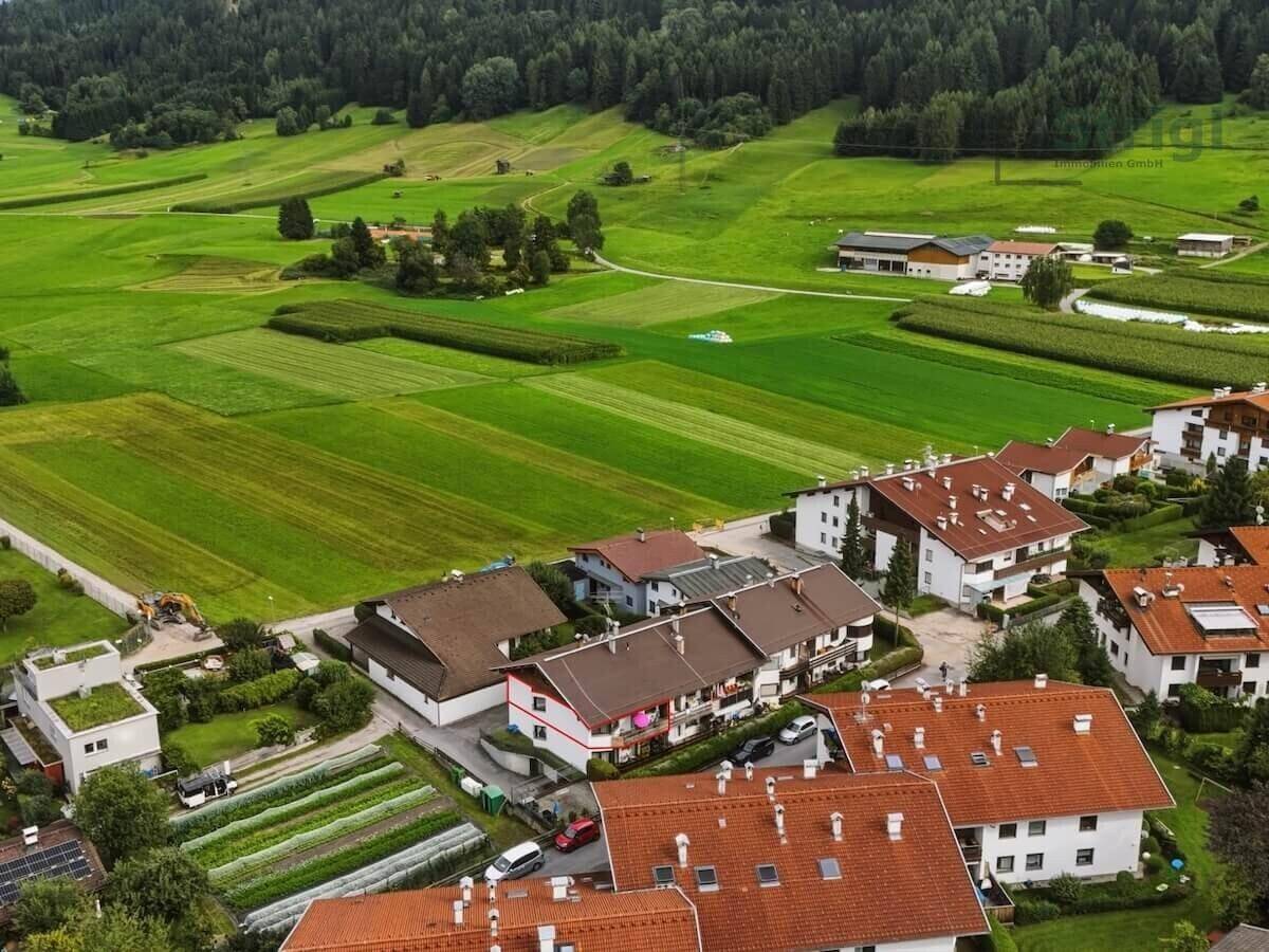 Luftaufnahme einer Wohnsiedlung umgeben von grünen Feldern und Bergen.