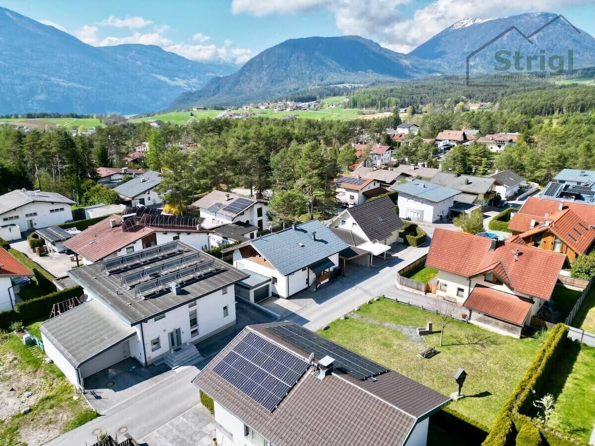Luftaufnahme der Wohnsiedlung mit vielen Häusern, Solaranlagen und majestätischen Bergen im Hintergrund.
