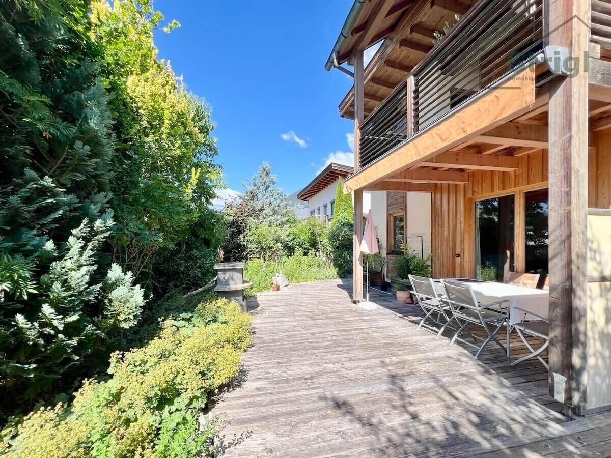 Geräumige Holzterrasse mit Esstisch und Stühlen, umgeben von grüner Bepflanzung.