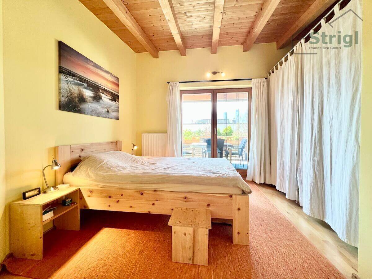 Schlafzimmer mit Holzbett, warmem Teppich und direktem Zugang zu einem Balkon oder einer Terrasse.