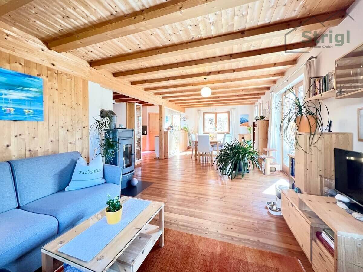 Gemütliches Wohnzimmer mit Holzbalkendecke, Kaminofen und offenem Übergang zum Essbereich.