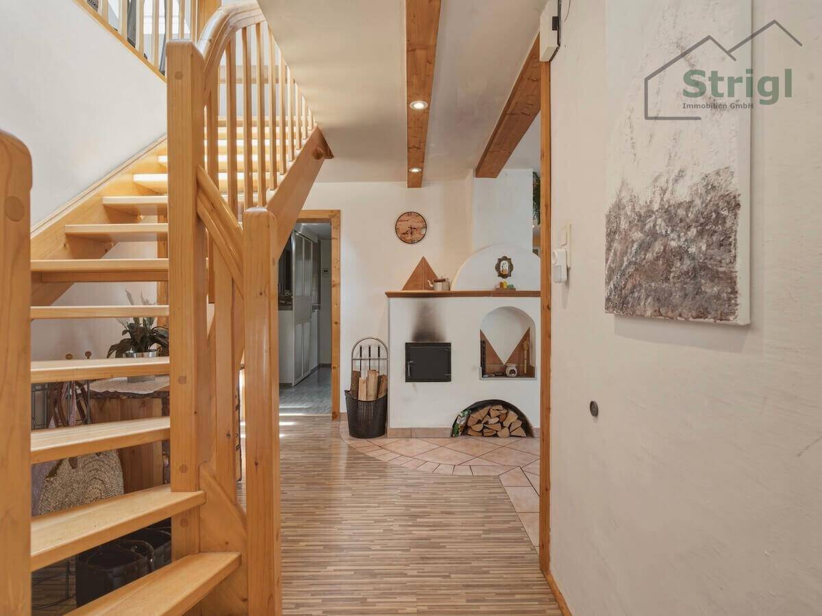 Gemütlicher Flur mit Holztreppe, Fliesenboden und einem traditionellen Kaminofen als Blickfang.