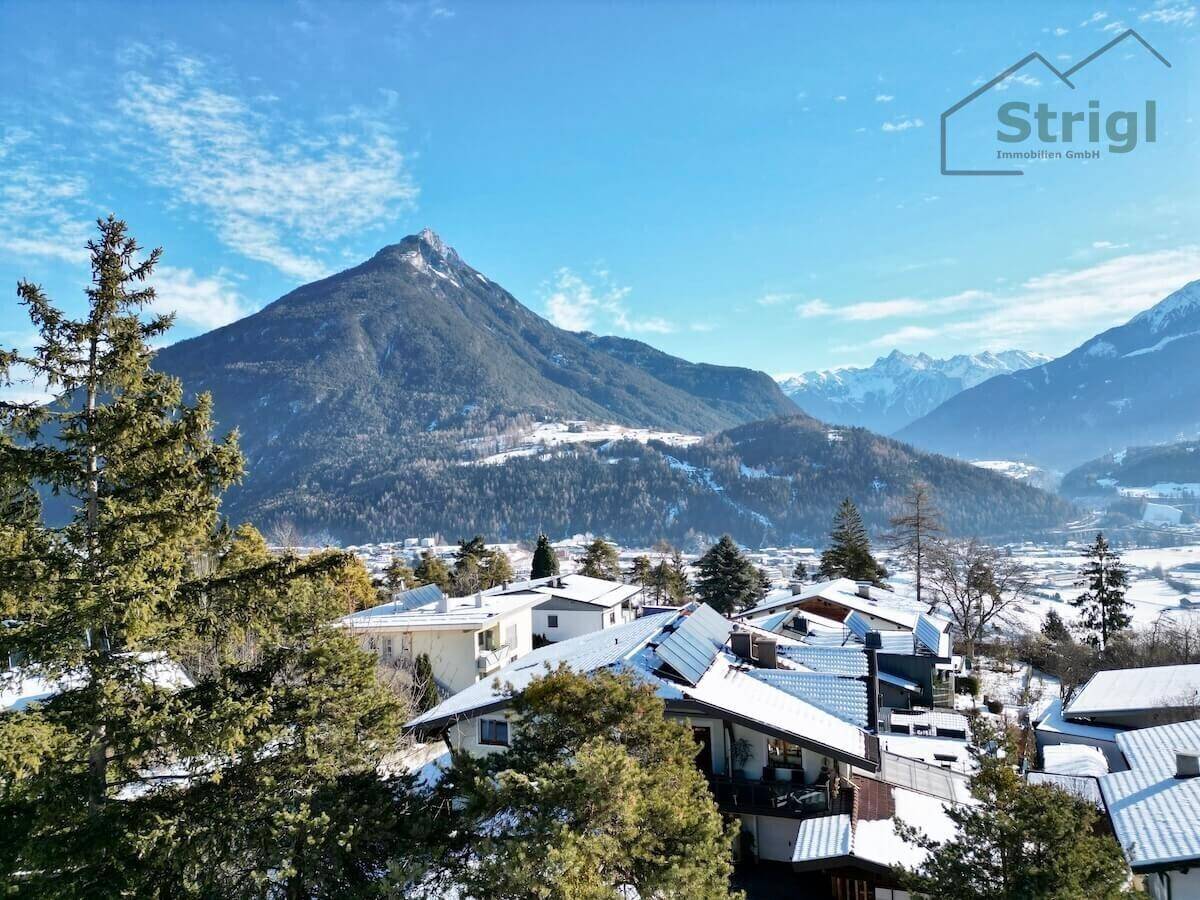 Panoramablick über eine verschneite Siedlung mit Häusern und majestätischen Bergen im Hintergrund.