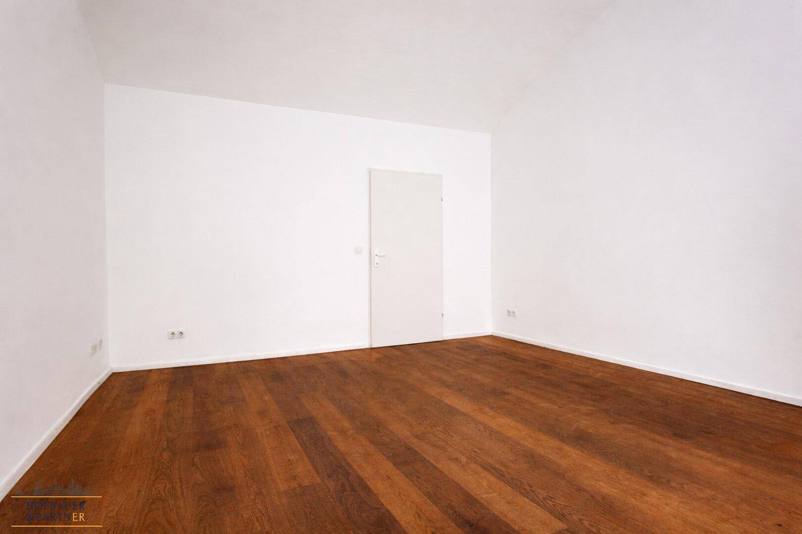 Leerer Raum mit Holzboden und weißen Wänden, ausgestattet mit einer einfachen Tür.