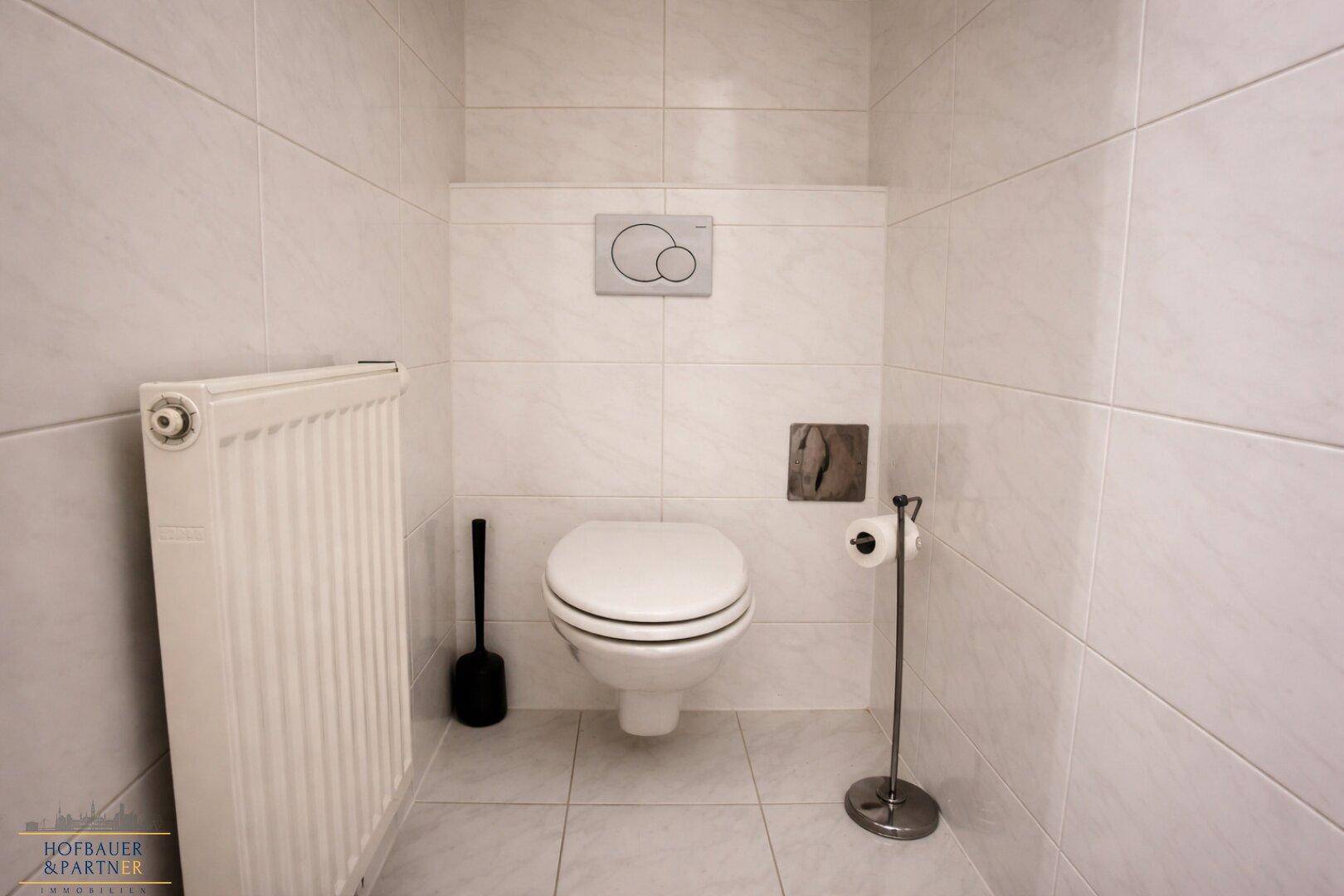 Gefliestes Gäste-WC mit wandhängendem WC und Heizkörper, in hellem und sauberem Zustand.