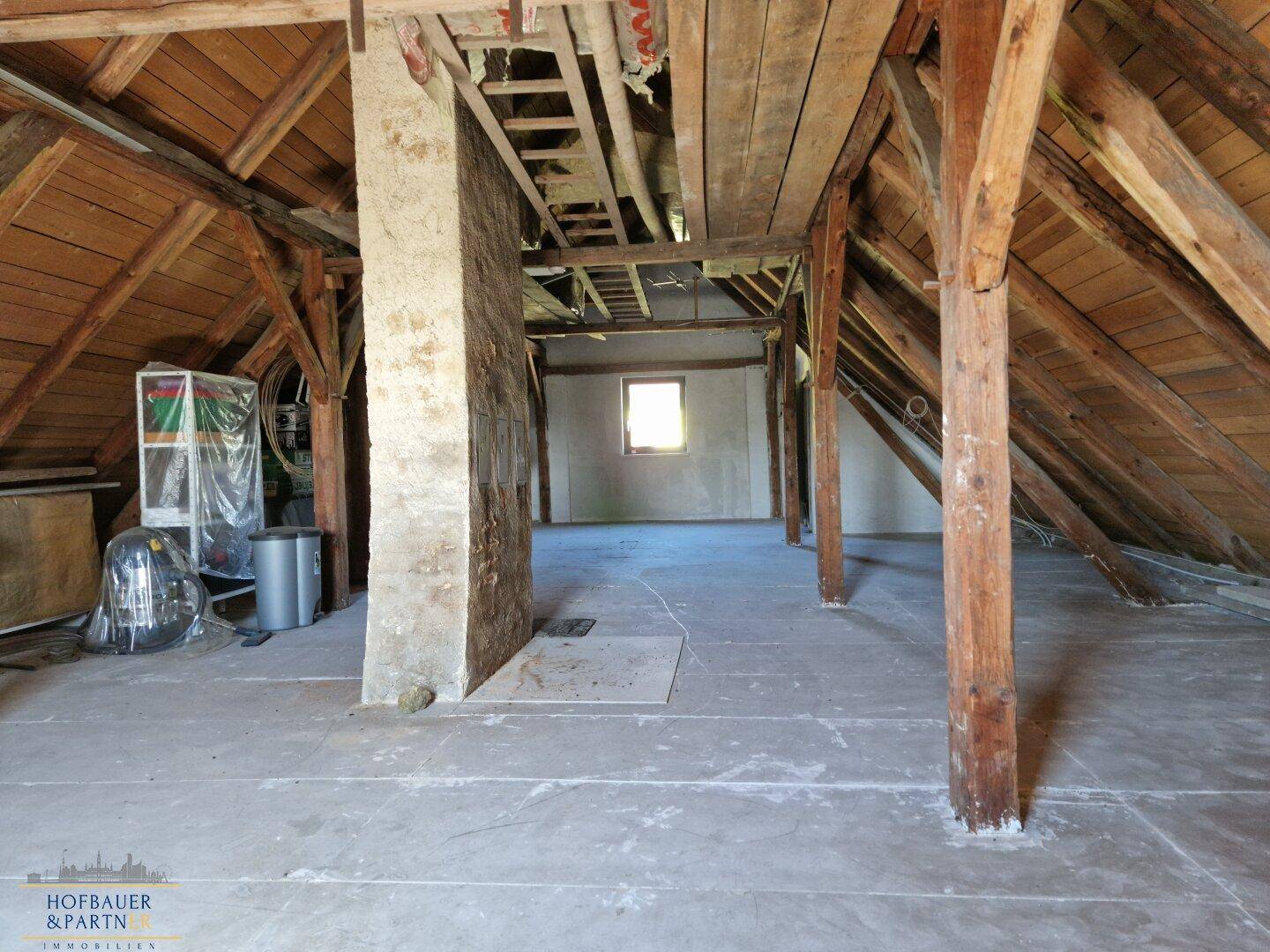 Unausgebauter Dachboden mit Holzbalken und Fenster, bietet Ausbaupotenzial.