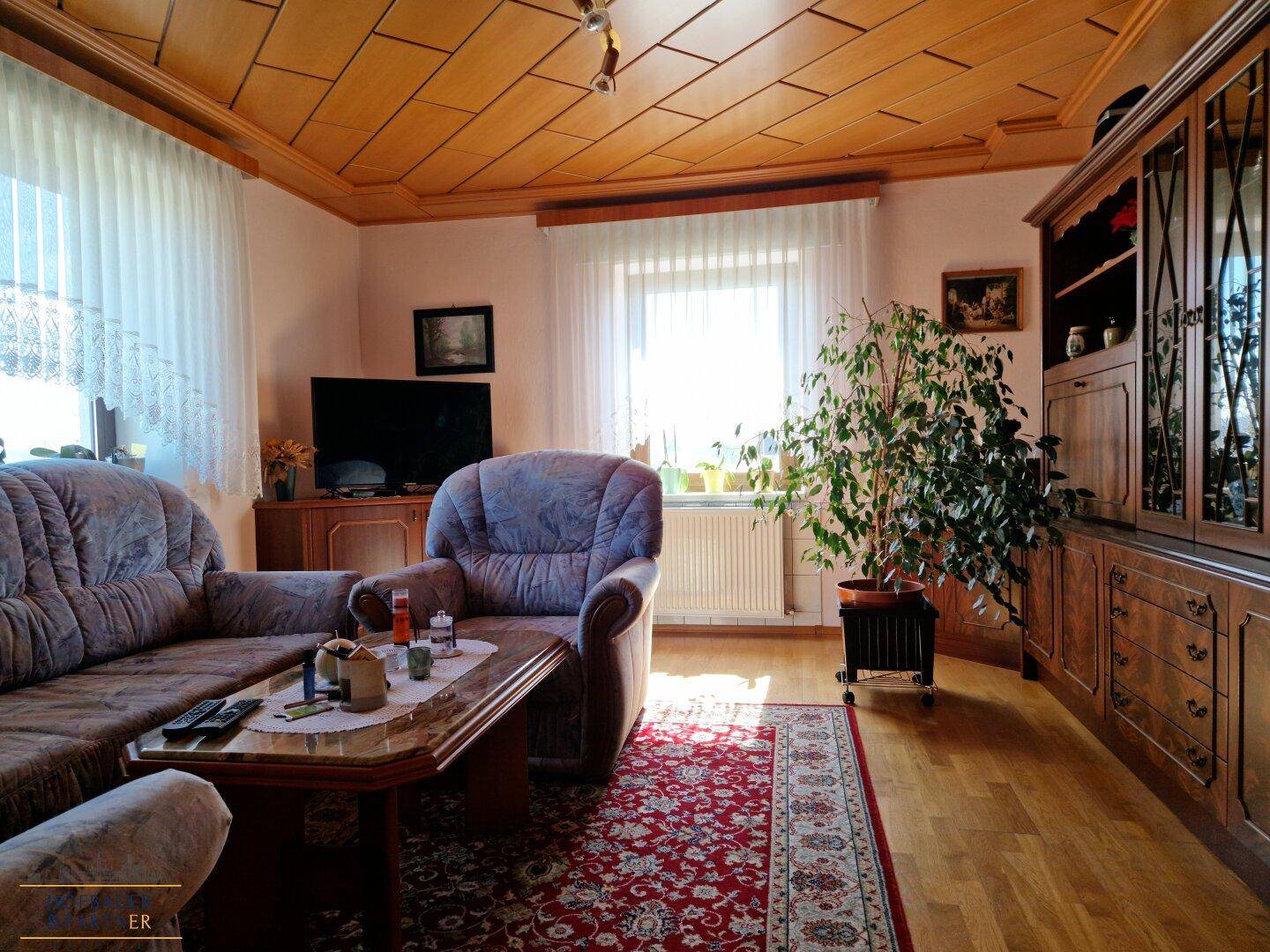 Gemütliches Wohnzimmer mit Holzdecke, Teppich und traditionellen Möbeln.