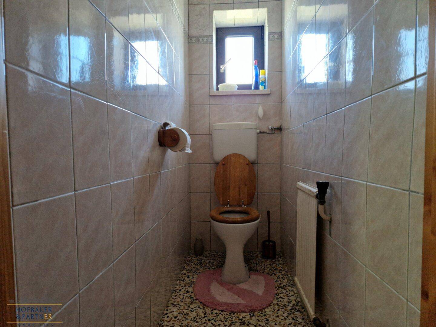 Kleines Gäste-WC mit Fliesen, Fenster und Holzdetails.