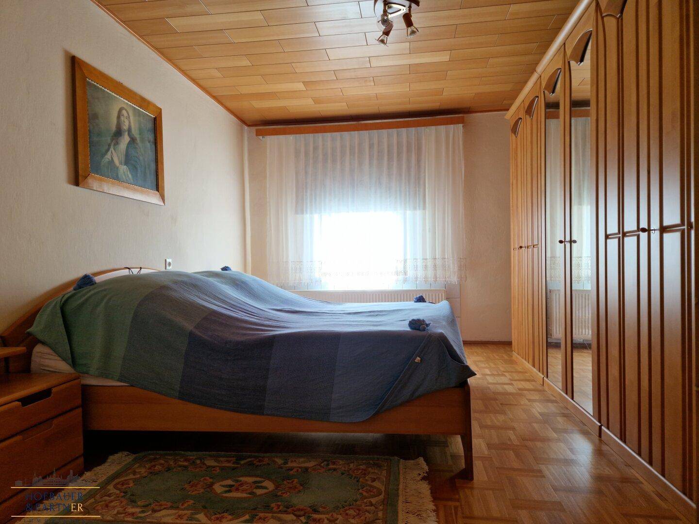 Helles Schlafzimmer mit Holzdecke, Parkettboden und großem Fenster.