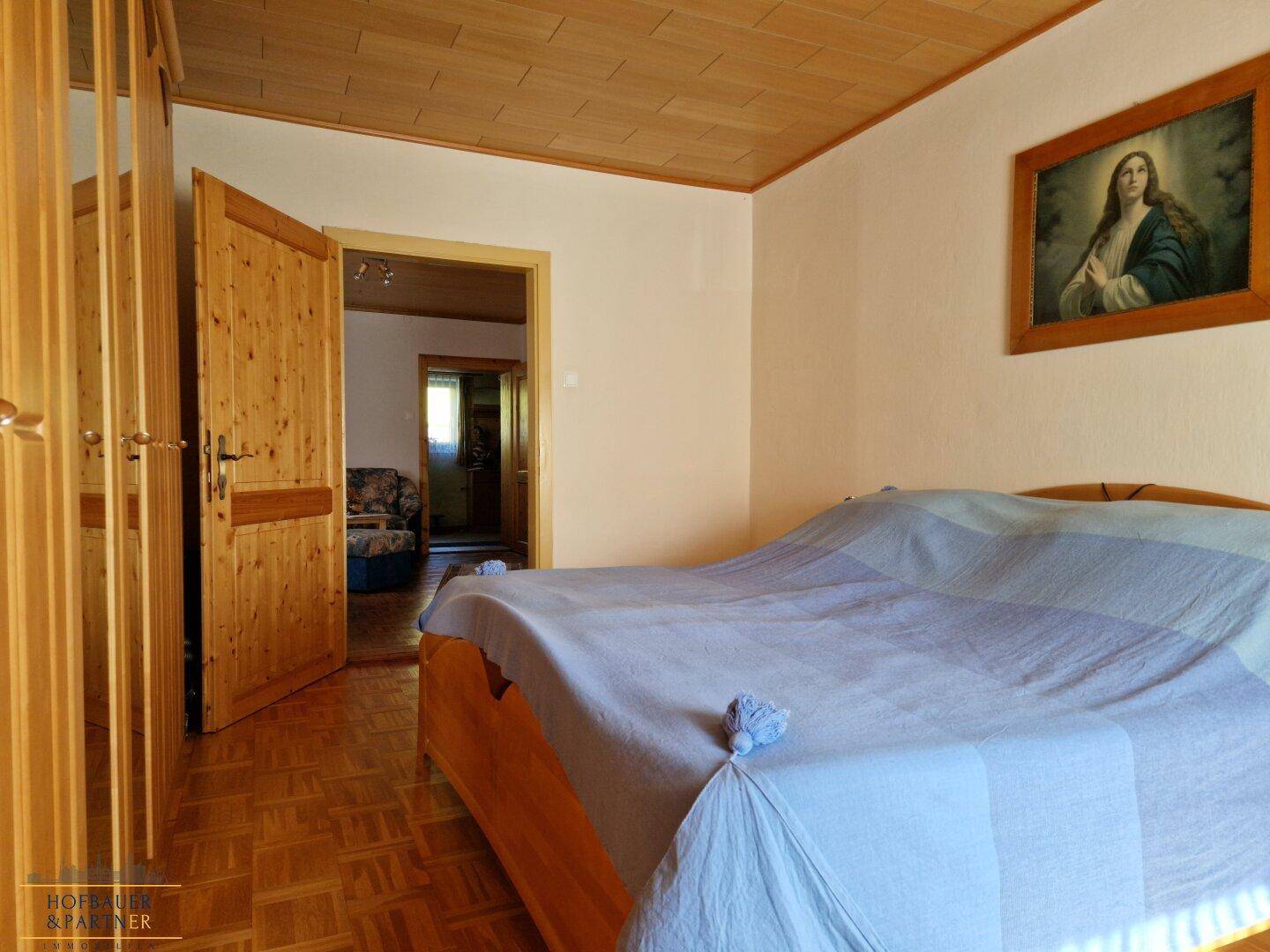 Schlafzimmer mit Holzmöbeln, Doppelbett und Zugang zu einem weiteren Raum.