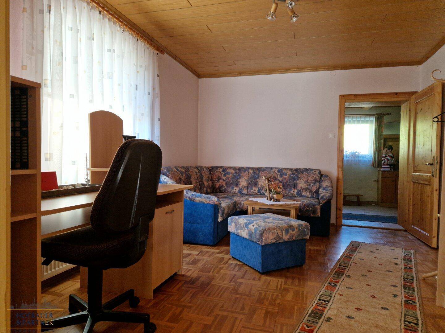 Wohnbereich mit Sofa, Schreibtisch und Zugang zu einem weiteren Zimmer.