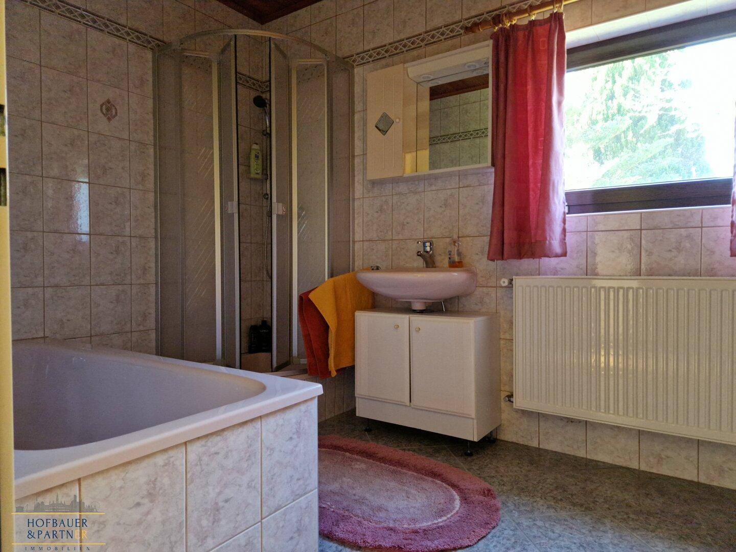 Gefliestes Badezimmer mit Badewanne, Dusche und Fenster.