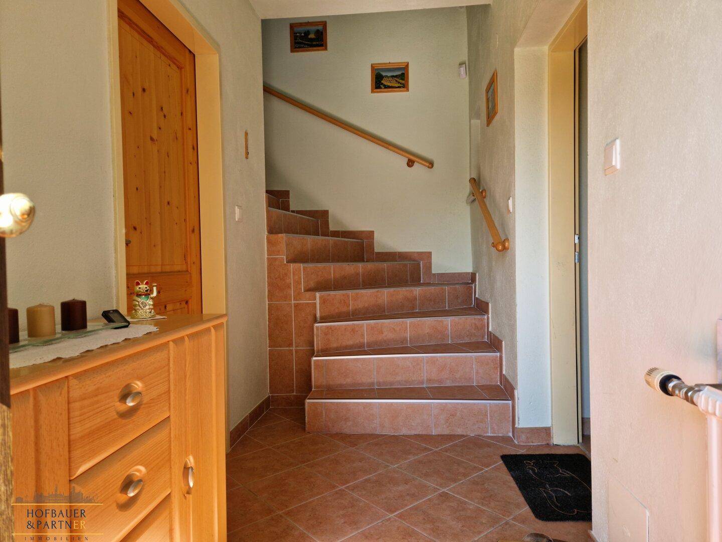 Gefliester Flur mit Treppe zum Obergeschoss und Holzmöbeln.