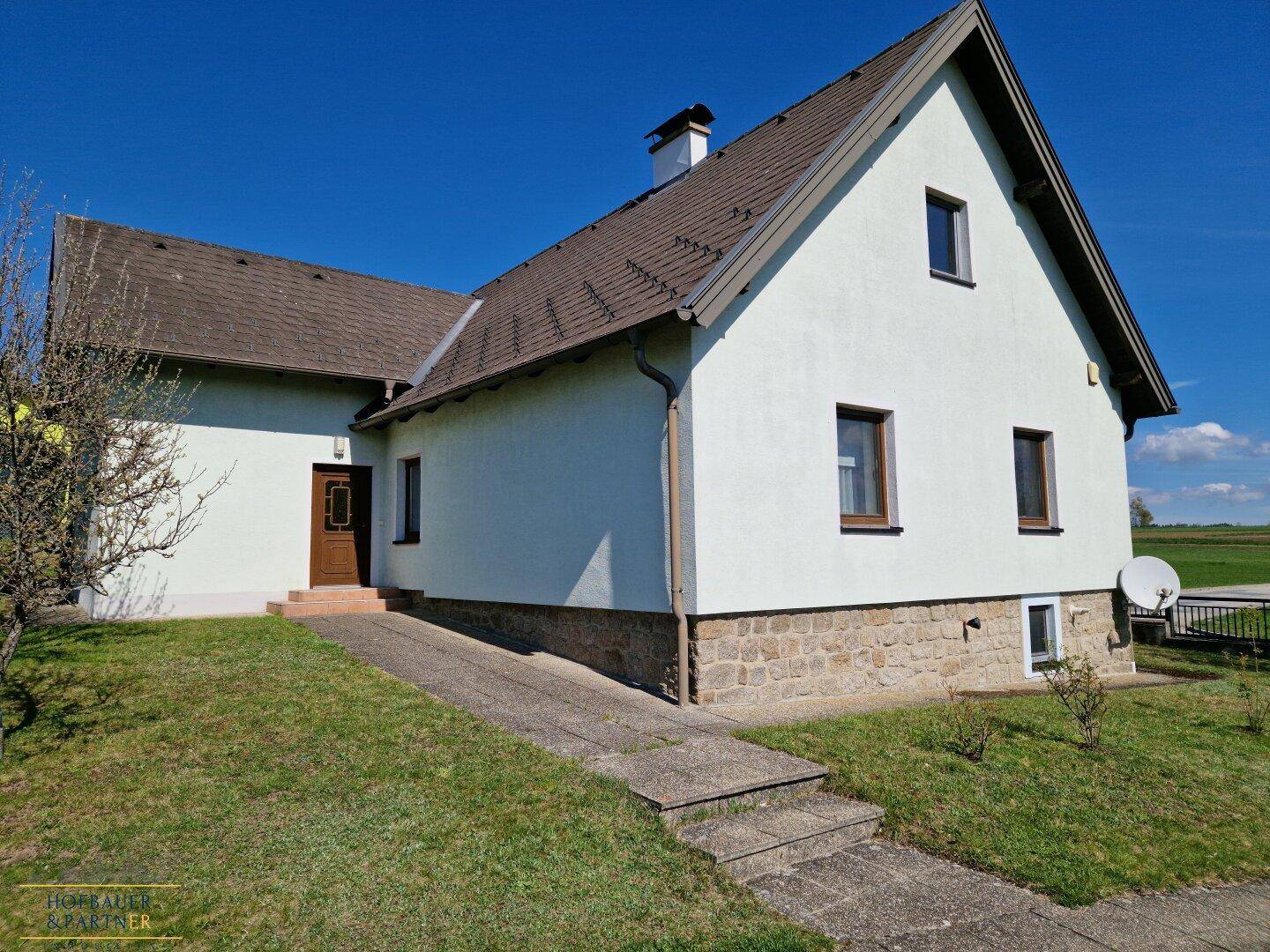 Einfamilienhaus mit weißer Fassade, Steinsockel und Zugang über eine Rampe.