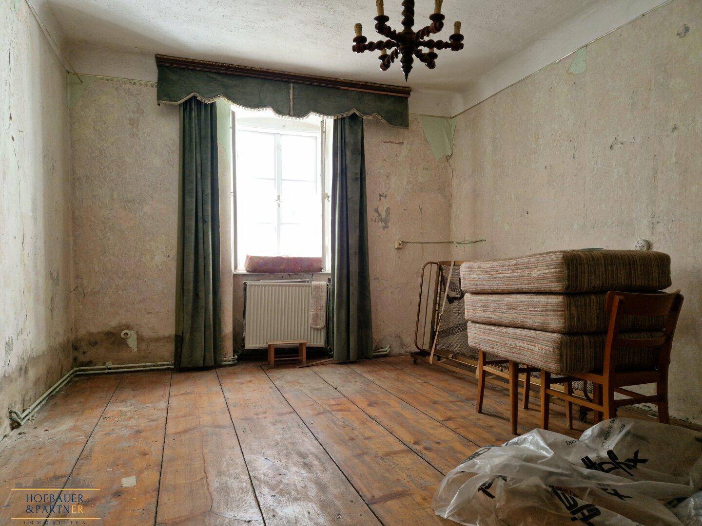 Leerer Raum mit abgenutzten Holzdielen, alten Tapeten und einem Fenster.