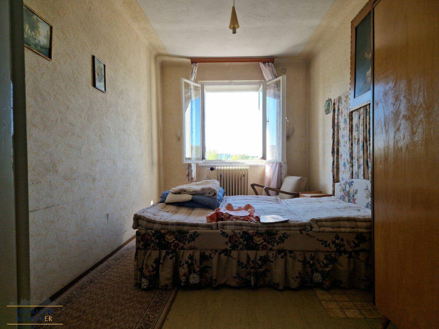 Schlafzimmer mit floraler Bettwäsche, Teppichboden und einem Fenster mit Ausblick.