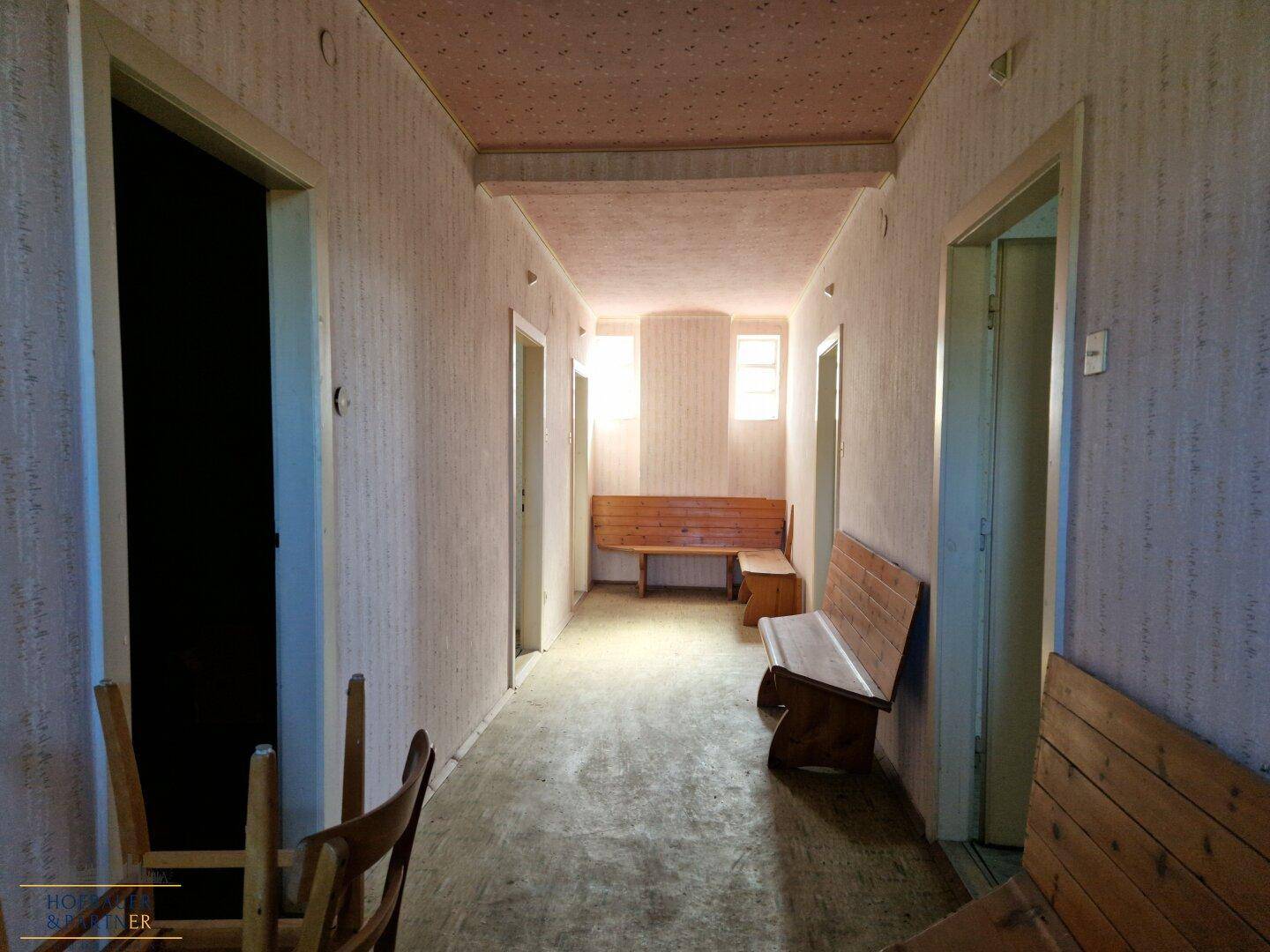 Langer Flur mit Holzbänken, alten Tapeten und mehreren Türen.