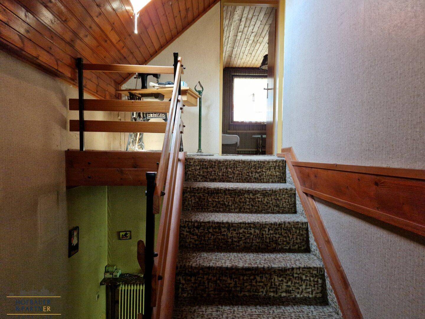 Treppenhaus mit Teppichboden, Holzgeländer und Blick auf den oberen Flur.