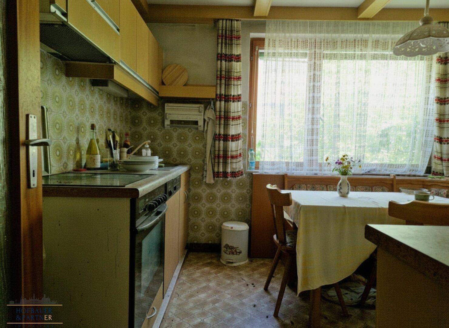 Funktionale Küche mit Einbaugeräten, Essbereich und Fenster mit Blick ins Grüne.