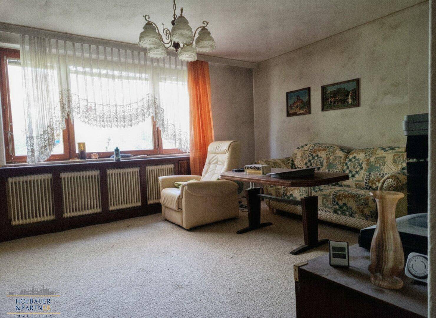 Helles Wohnzimmer mit gemütlicher Sitzecke, Teppichboden und Blick ins Grüne.
