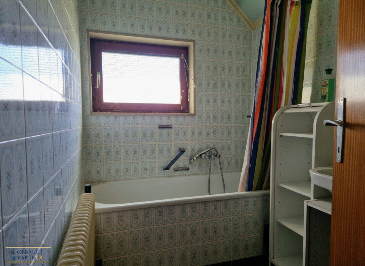 Badezimmer mit Badewanne, blauen Fliesen und Fenster für natürliche Belüftung.