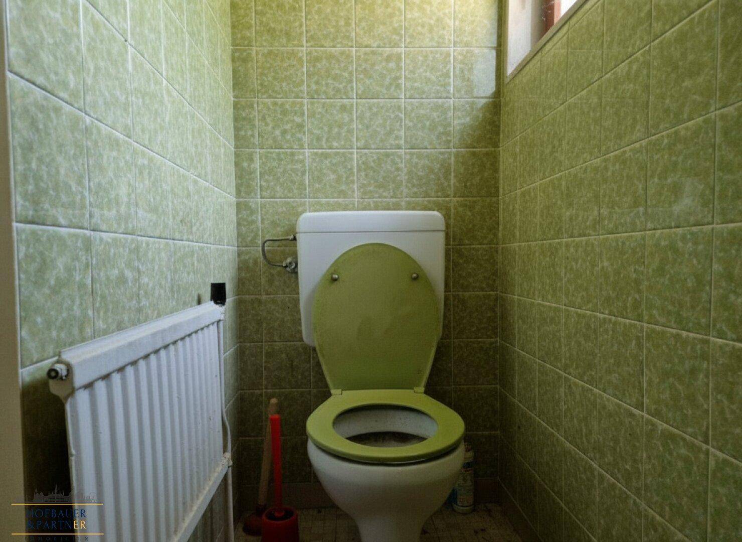 Separate Toilette mit grünen Fliesen, Heizkörper und Fenster für Belüftung.