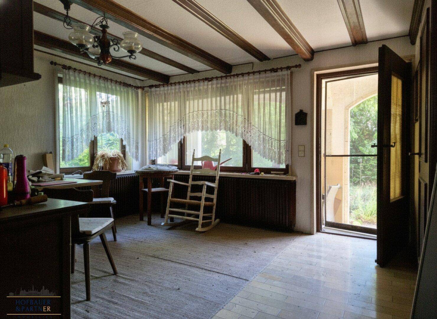 Wohnzimmer mit Holzbalkendecke, großen Fenstern und direktem Zugang zur Terrasse.