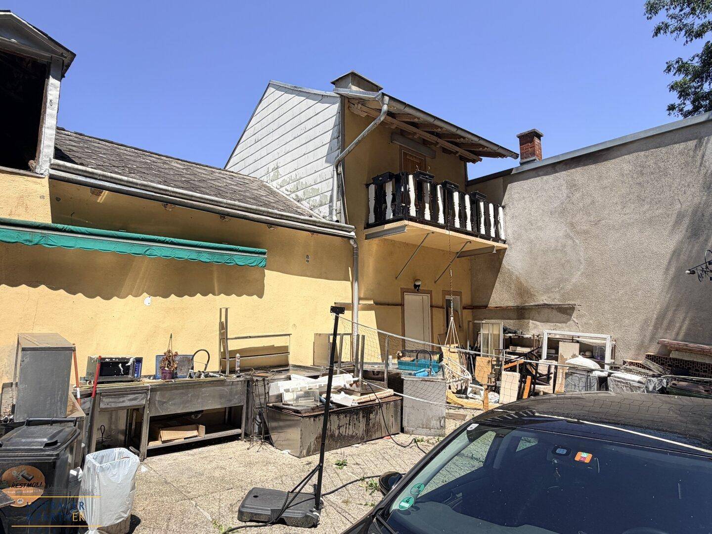 Rückseite des Gebäudes mit einem kleinen Balkon und einem unaufgeräumten Außenbereich.