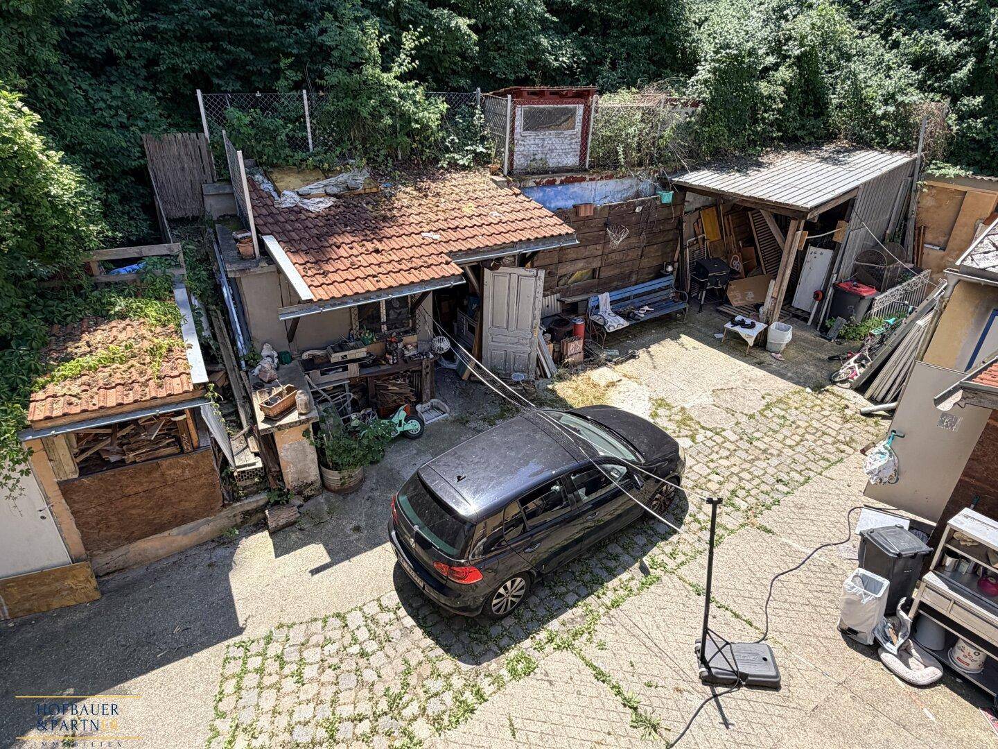Innenhof mit gepflastertem Bereich, einem geparkten Auto und verschiedenen Nebengebäuden.