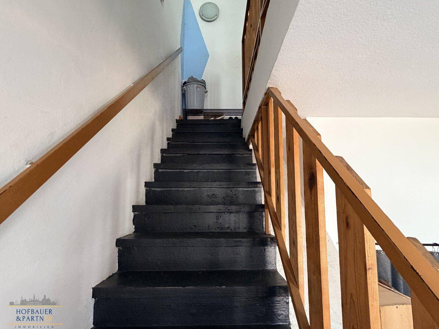 Treppenaufgang mit Holzgeländer und dunklen Stufen, führt in die obere Etage.