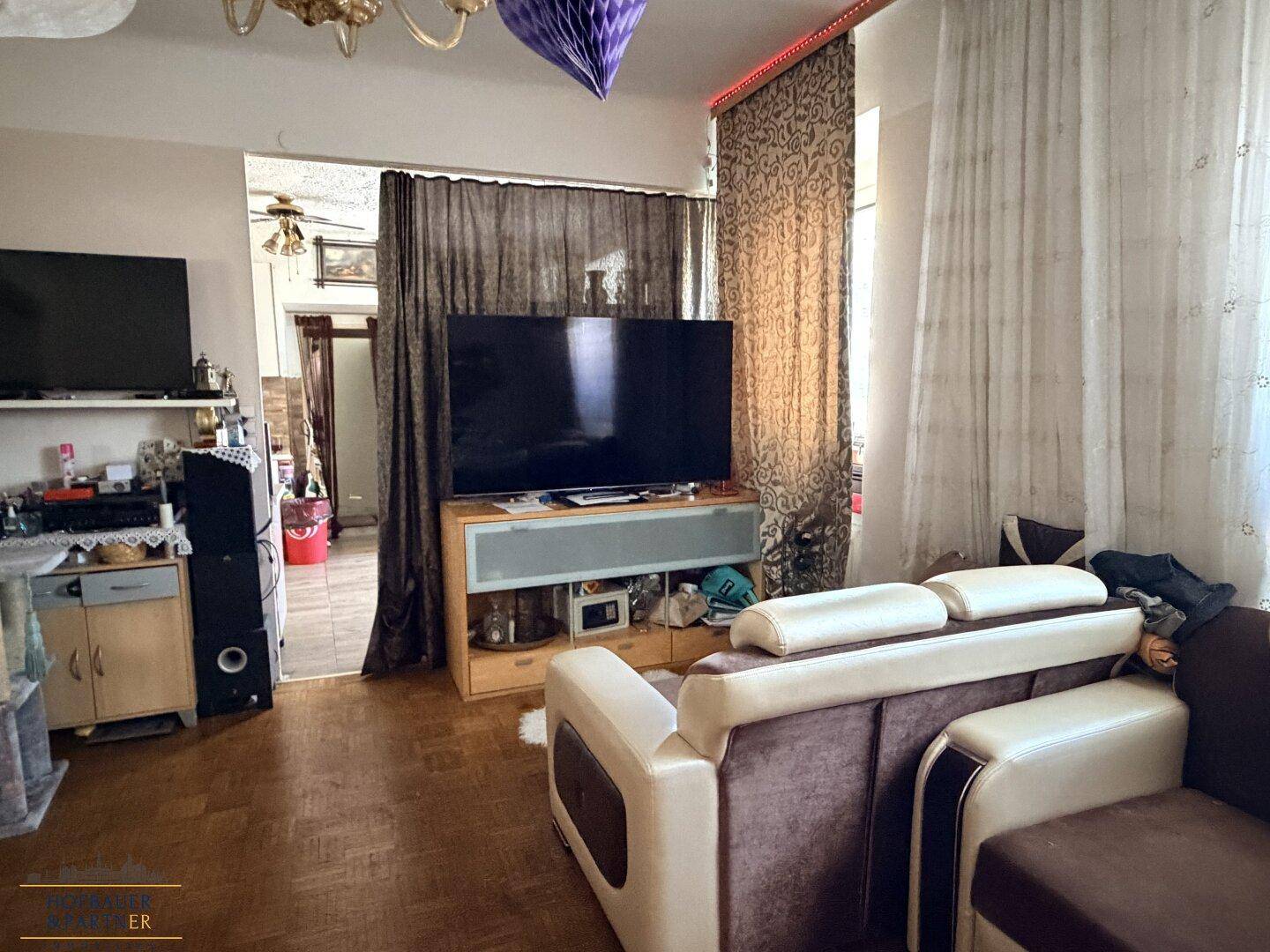 Gemütlicher Wohnzimmerbereich mit großem Fernseher, bequemen Sofas und Parkettboden.