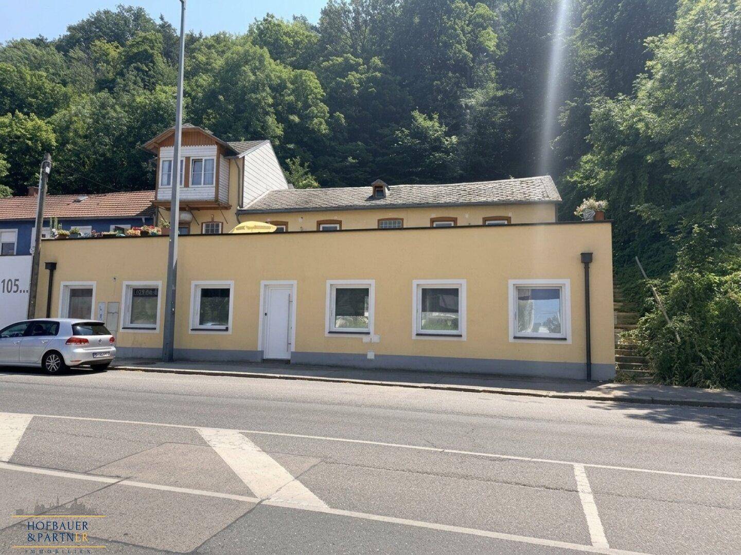 Ansicht des Gebäudes von der Straße aus mit gelber Fassade und umgebender grüner Landschaft.