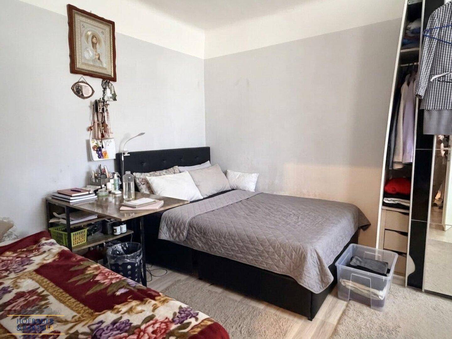 Schlafzimmer mit zwei Betten, einem Schreibtisch und einem offenen Kleiderschrank.
