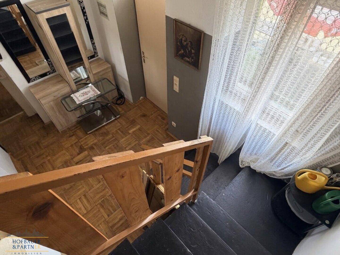 Treppenabgang mit Holzgeländer und Parkettboden im unteren Bereich, hell durch Fenster.