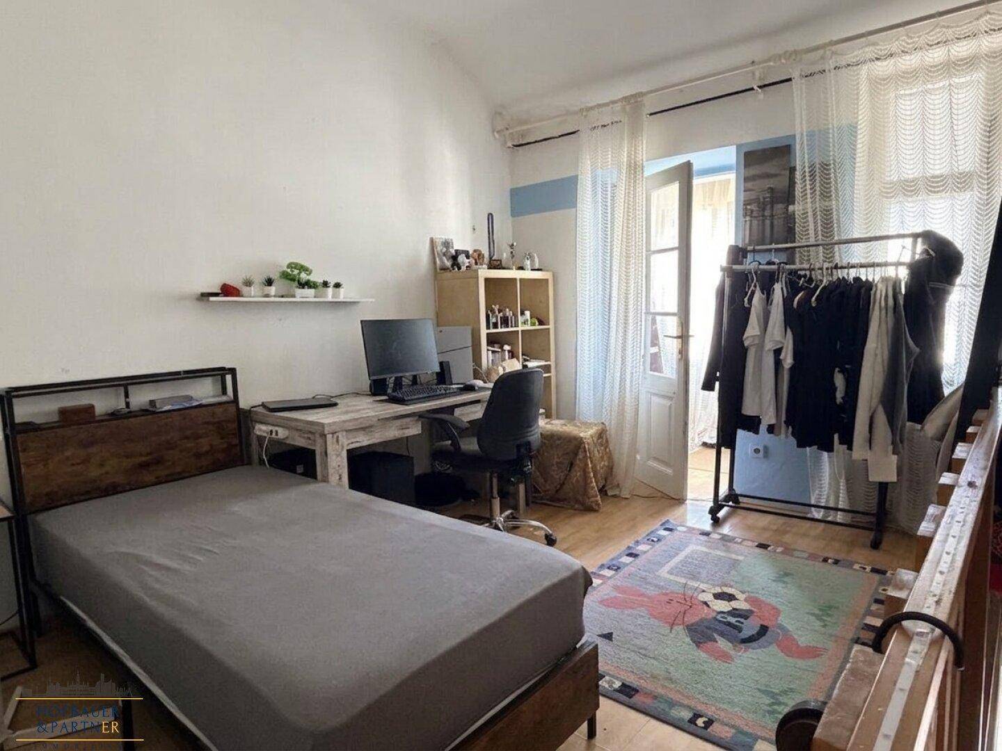 Schlafzimmer mit Schreibtisch, Holzfußboden und Zugang zu einem Balkon oder einer Terrasse.