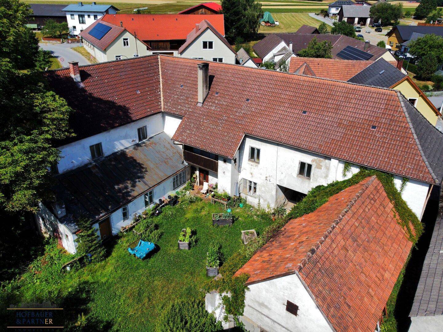 Vogelperspektive des Anwesens mit dem grünen Gartenbereich, den Nebengebäuden und den roten Ziegeldächern.