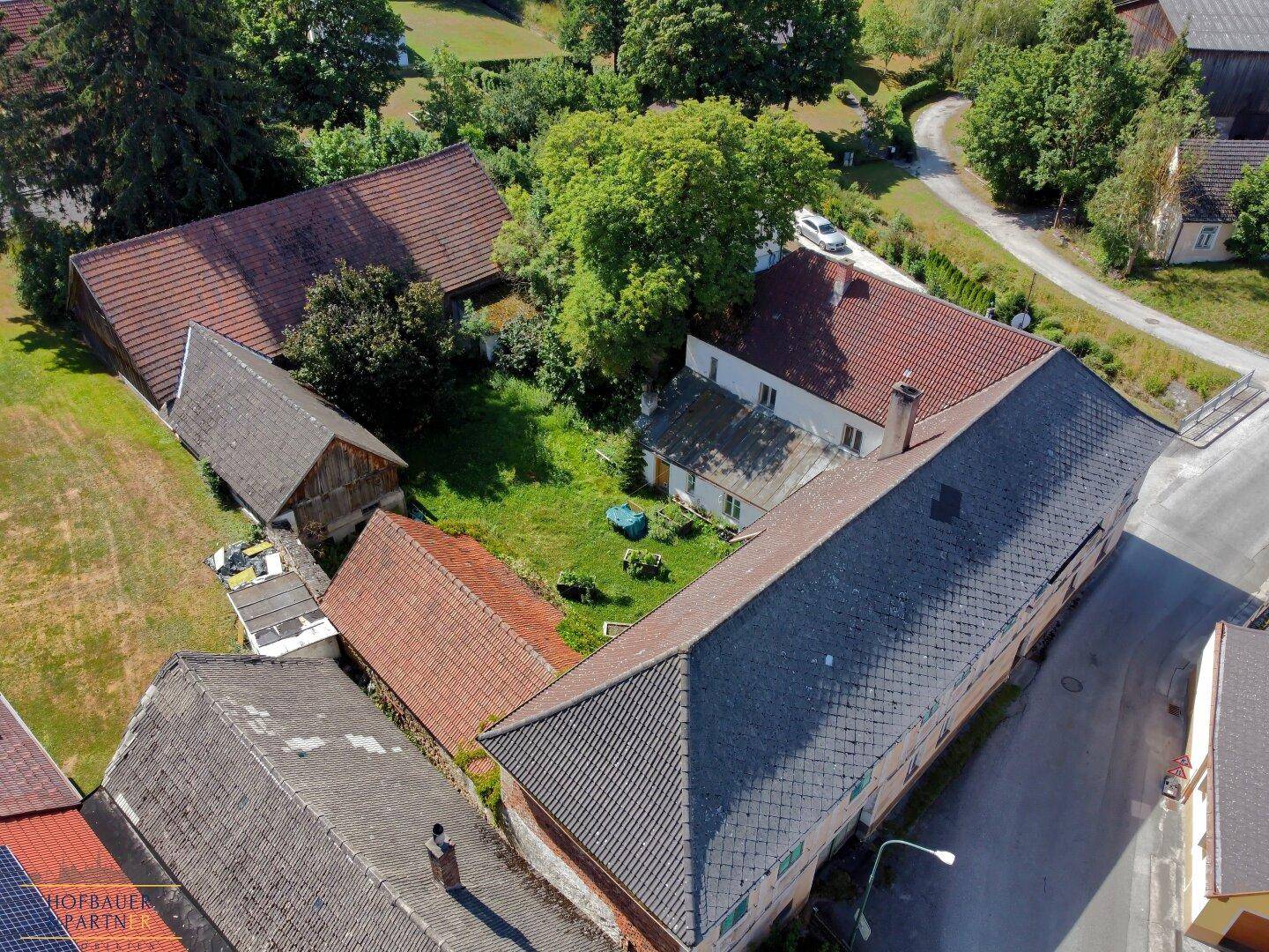 Luftaufnahme des weitläufigen Anwesens mit mehreren Gebäuden, verschiedenen Dächern und einem großen Innenhof.