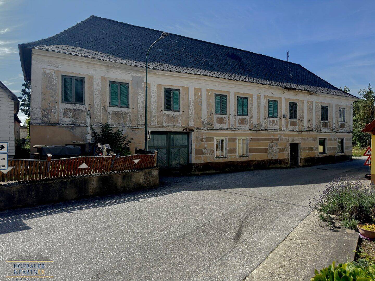 Seitenansicht des alten Gebäudes mit großem Holztor, verwitterter Fassade und traditionellem Ziegeldach.