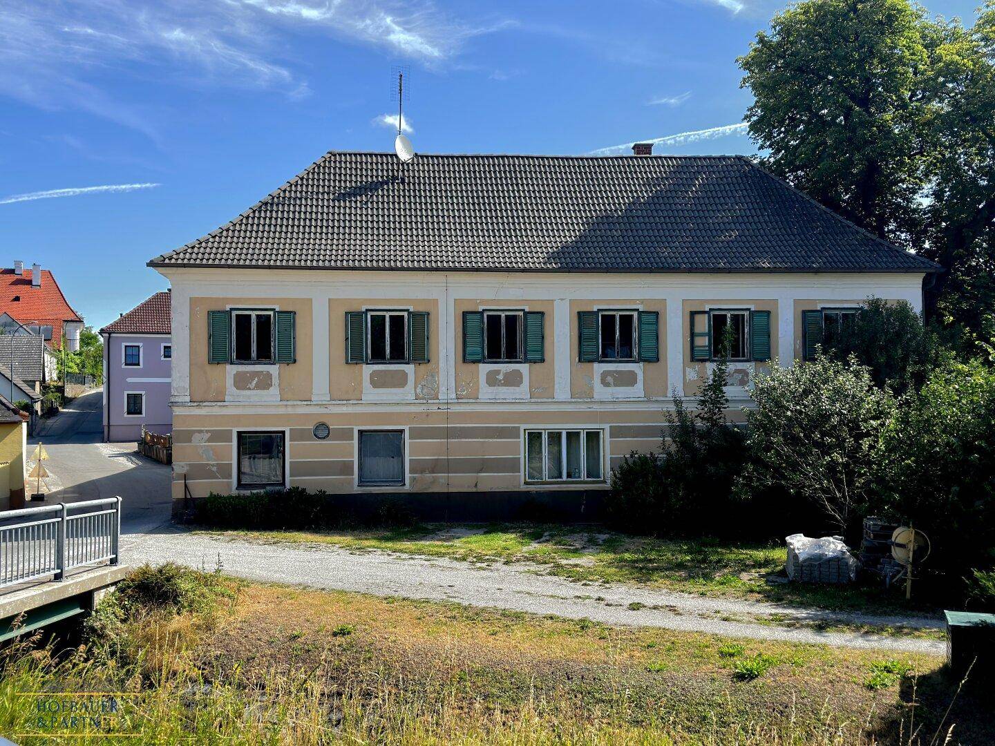 Vorderansicht des historischen Gebäudes mit symmetrischen Fenstern, grünen Fensterläden und einem traditionellen Ziegeldach.