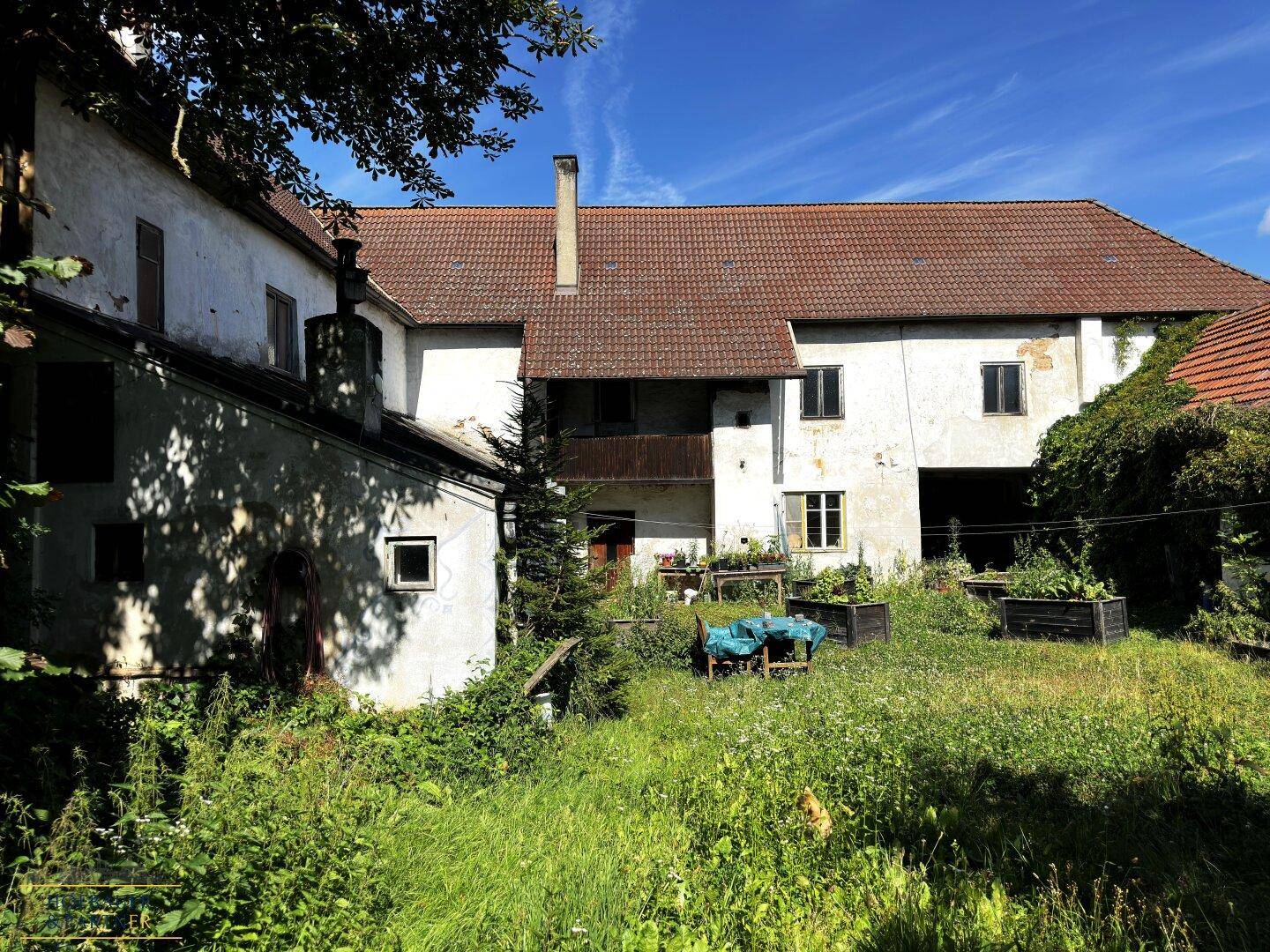 Blick auf den weitläufigen, grünen Garten mit alten Gebäuden und einem kleinen Balkon im ländlichen Ambiente.