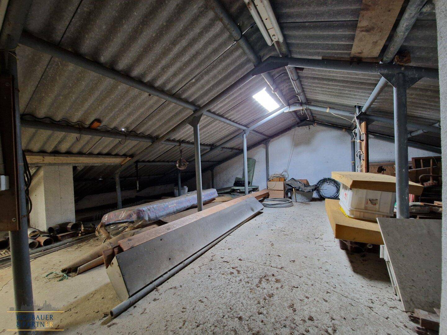 Unausgebauter Dachboden mit sichtbaren Balken und Dachfenster.