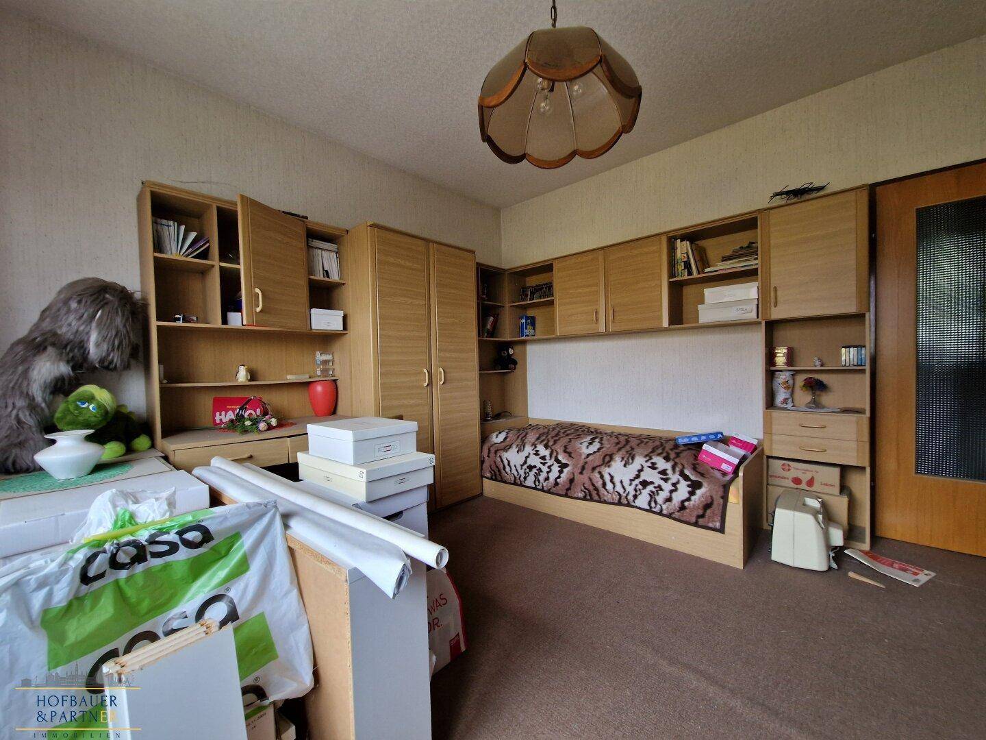 Schlafzimmer mit Einzelbett, Holzmöbeln und Stauraum.