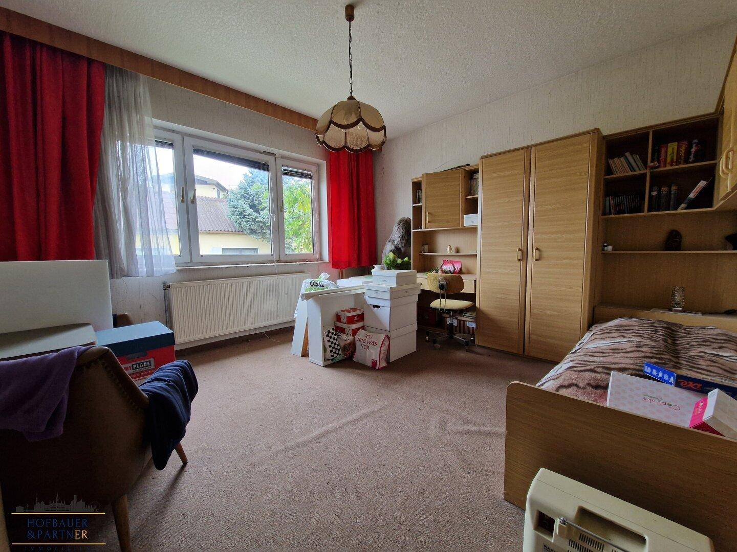 Schlafzimmer mit Teppichboden, Holzmöbeln und roten Vorhängen.