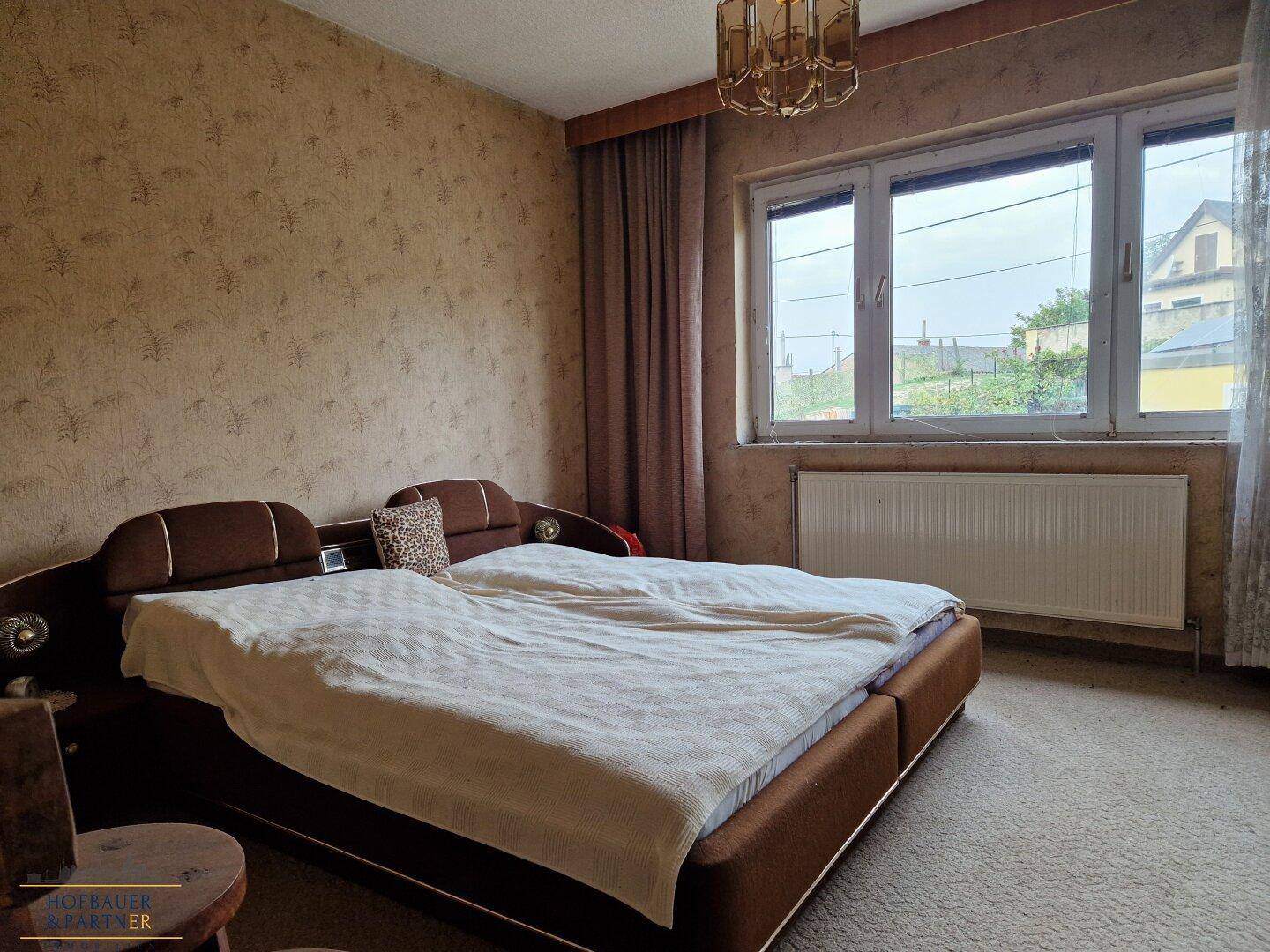 Schlafzimmer mit Doppelbett, Teppichboden und gemusterter Tapete.