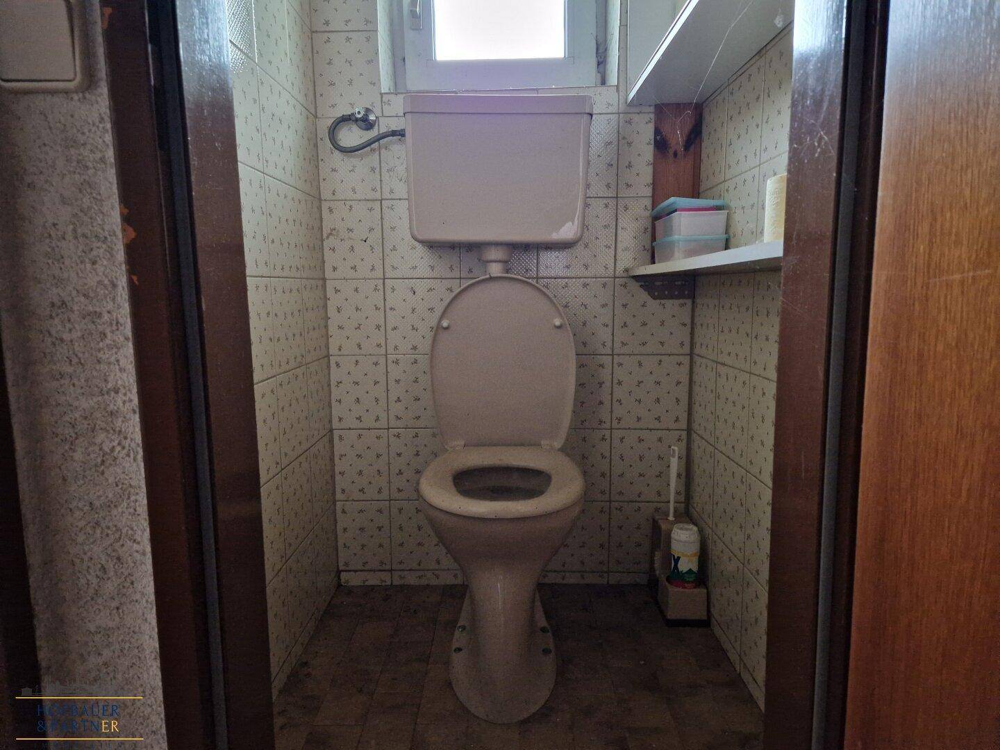 Kleines WC mit Toilette, Fliesen und Fenster.